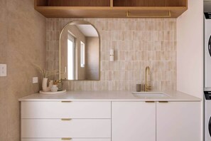 A bathroom with a white vanity, a gold faucet, a mirror with an arch design, and a tiled backsplash.