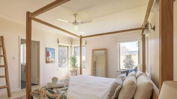 Ein Schlafzimmer mit einem Himmelbett, einem Deckenventilator, einem Fenster mit Jalousien und einer Holzleiter.