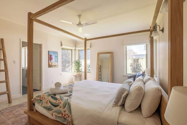 A bedroom with a four-poster bed, a ceiling fan, a window with blinds, and a wooden ladder.