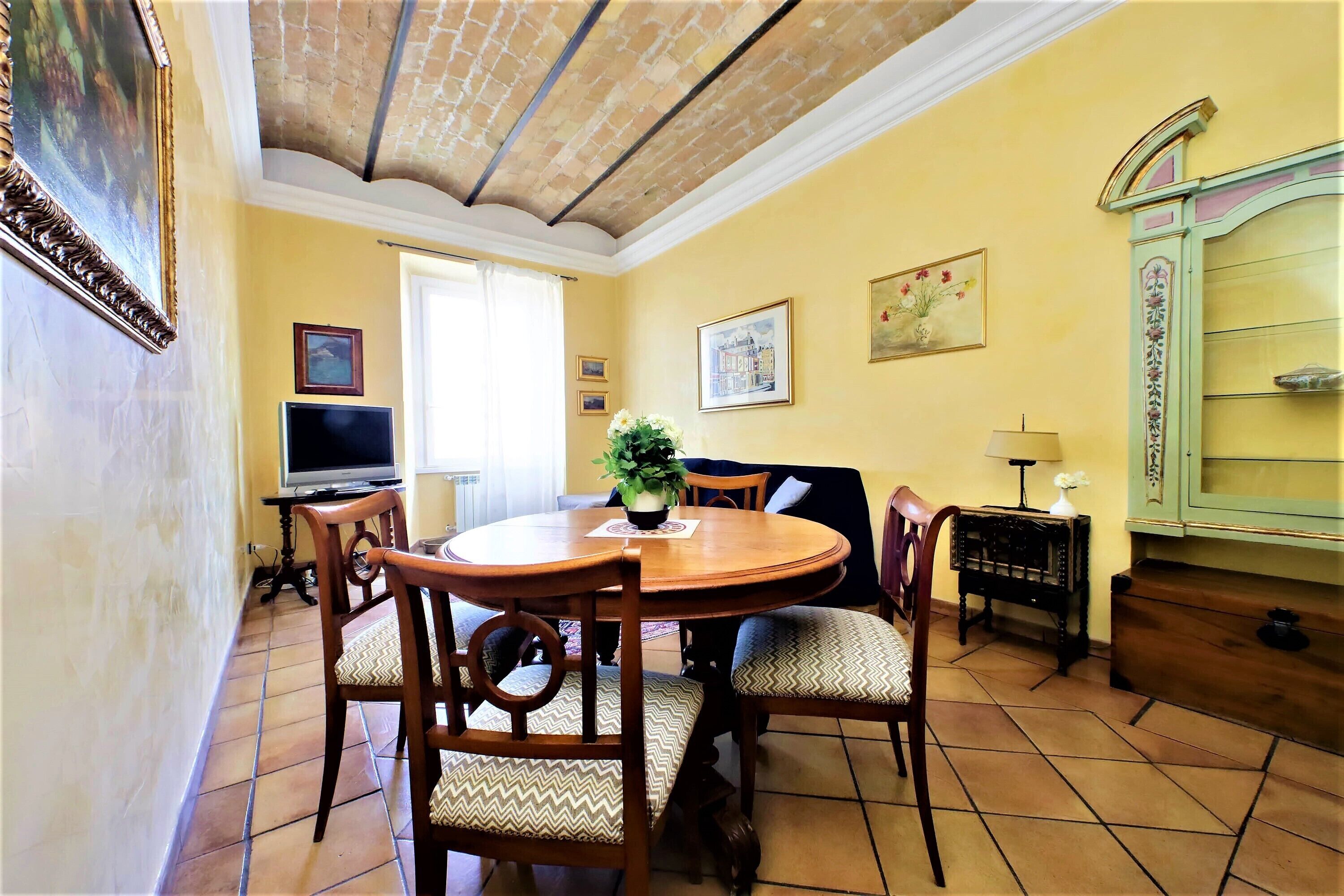 A dining area with a round wooden table, four chairs, a television, and a cabinet with a decorative top.