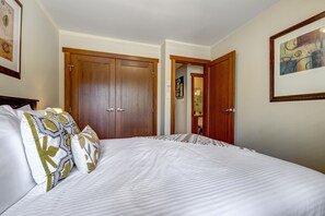 A bedroom with a large bed, two doors, and a bathroom visible through an open door.