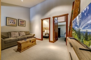 A living room with a sofa, coffee table, and a painting of a forest. - Telemark 23 - Ski in Walk out, Private Sauna, Short Walk to the Village (Whistler)