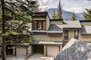 A two-story house with a stone foundation, a garage, and a view of mountains in the background. - Telemark 23 - Ski in Walk out, Private Sauna, Short Walk to the Village (Whistler)
