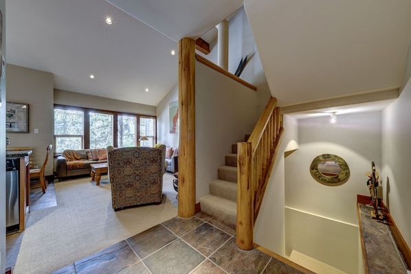 A spacious living area with a sofa, a patterned armchair, and a staircase with wooden railings. - Telemark 23 - Ski in Walk out, Private Sauna, Short Walk to the Village (Whistler)