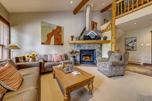 A cozy living room with a fireplace, a sofa, a coffee table, and a patterned armchair.