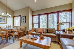 A well-lit living room with a dining area, large windows, and a chandelier.