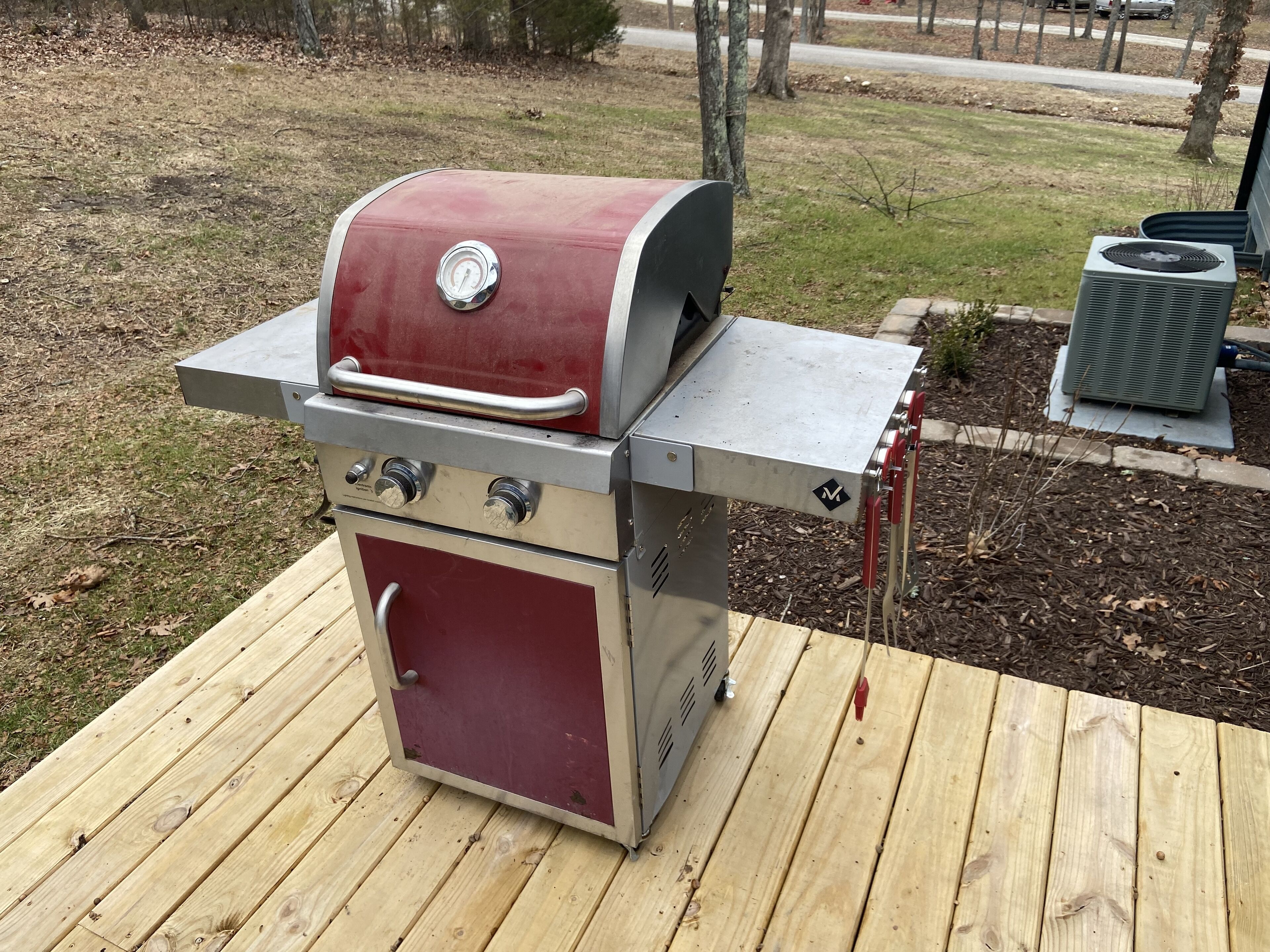 A stainless steel and red barbecue grill with a digital thermometer, a side burner, and a chimney starter.