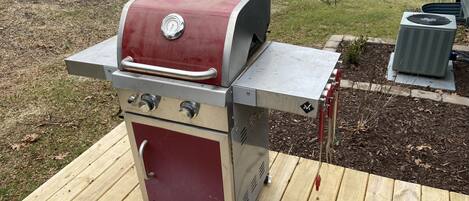 A stainless steel and red barbecue grill with a digital thermometer, a side burner, and a chimney starter.