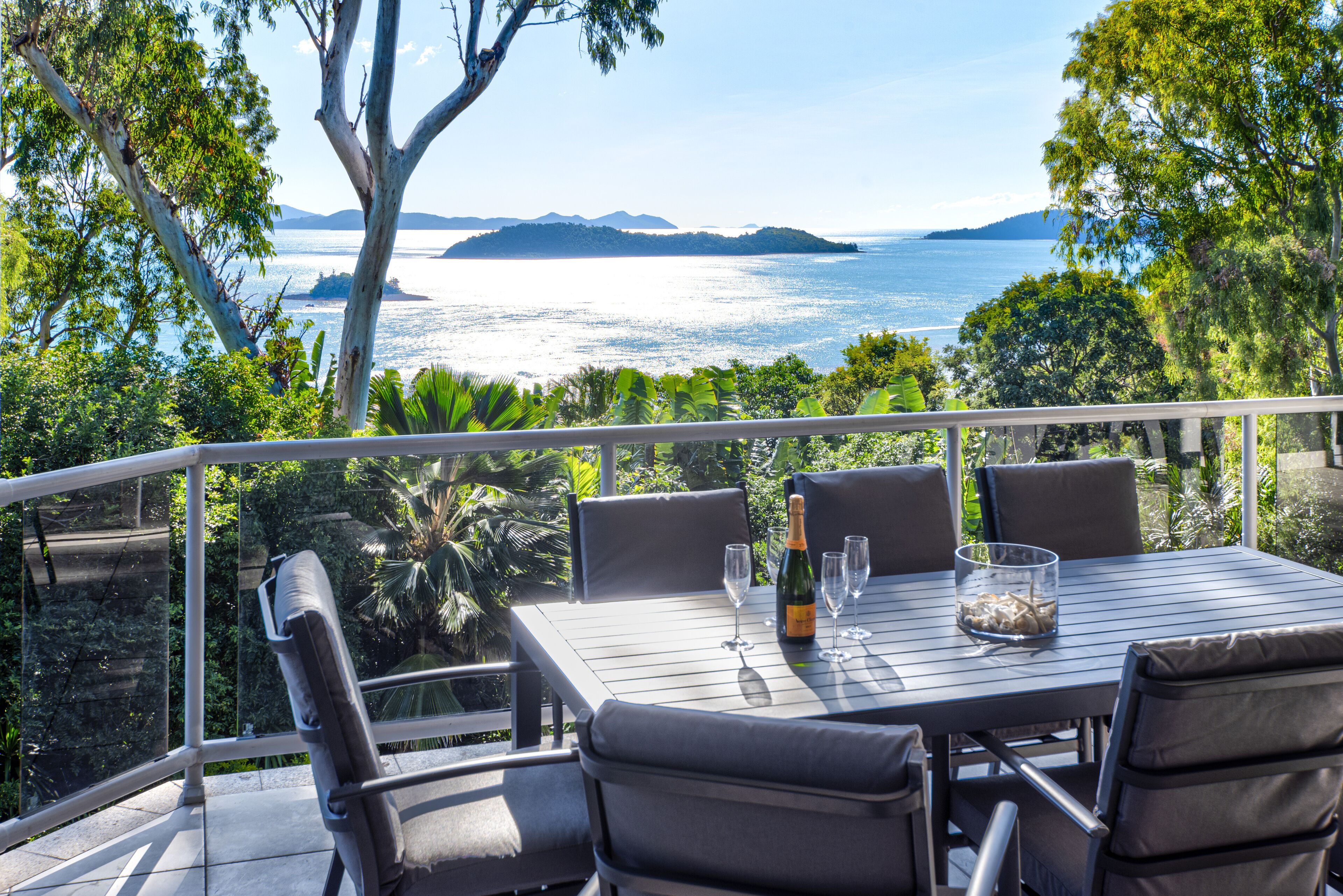 Area pranzo all'aperto con tavolo apparecchiato per due, con vista panoramica sul mare e isole sullo sfondo.