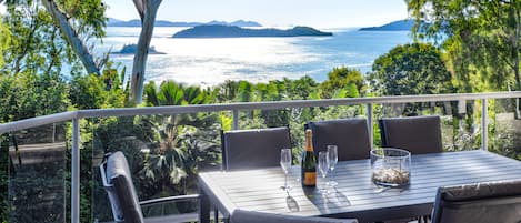 Un espace de restauration en plein air avec une table dressée pour deux personnes, offrant une vue panoramique sur la mer et les îles lointaines.