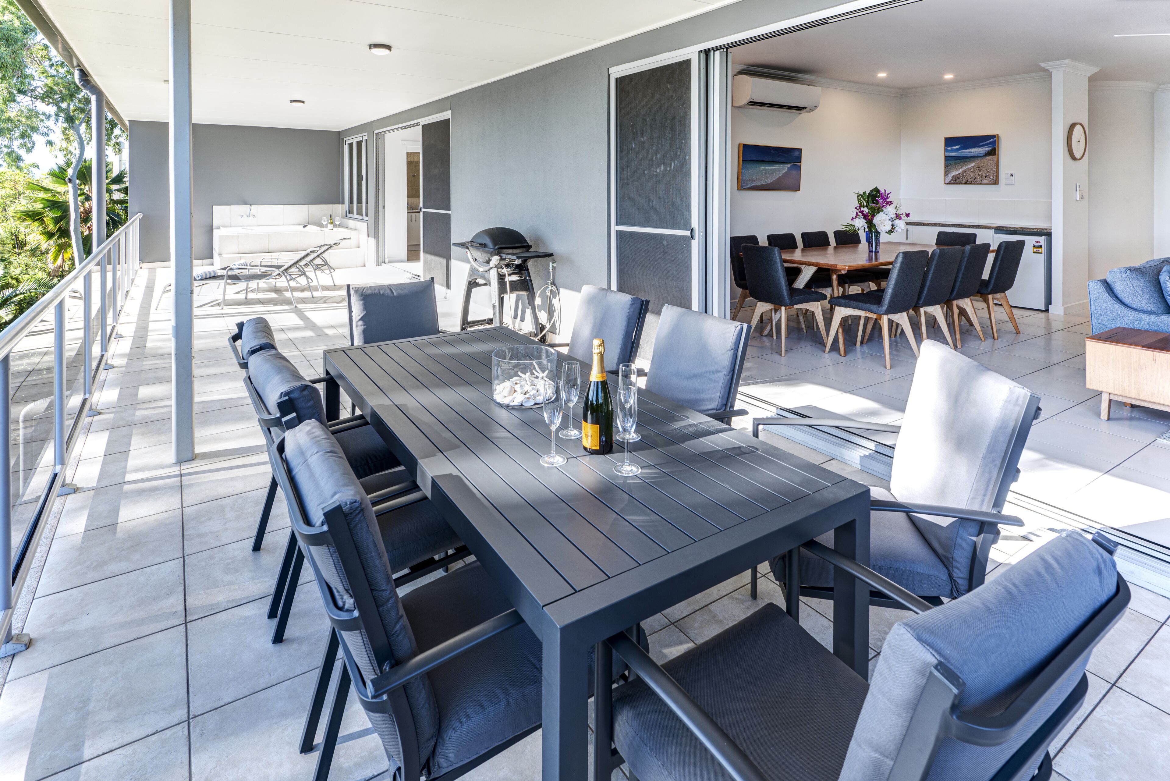 Un espace extérieur moderne aménagé pour les repas, avec une longue table, des chaises et un barbecue.