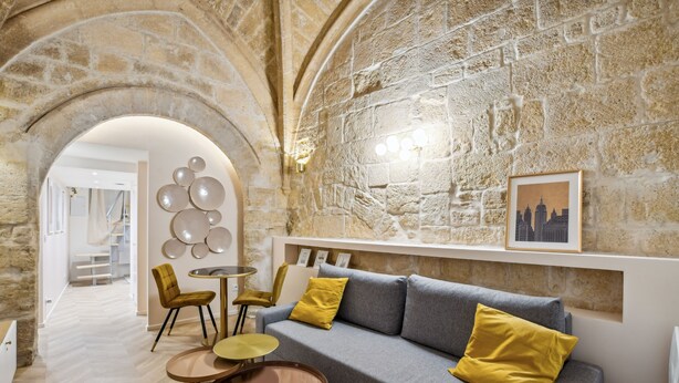 A modern interior with a stone wall, a grey sofa with yellow cushions, and a round table with chairs. - Beautiful and very quiet historical apartment located in the hyper center (Montpellier)