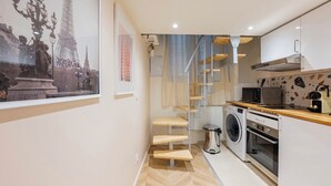 A compact kitchen with a washing machine, oven, and a microwave. A staircase leads to a balcony with a view of the Eiffel Tower. - Beautiful and very quiet historical apartment located in the hyper center (Montpellier)