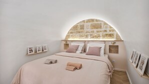 A bedroom with a stone arch window, a bed with beige bedding, and framed pictures on the wall. - Beautiful and very quiet historical apartment located in the hyper center (Montpellier)