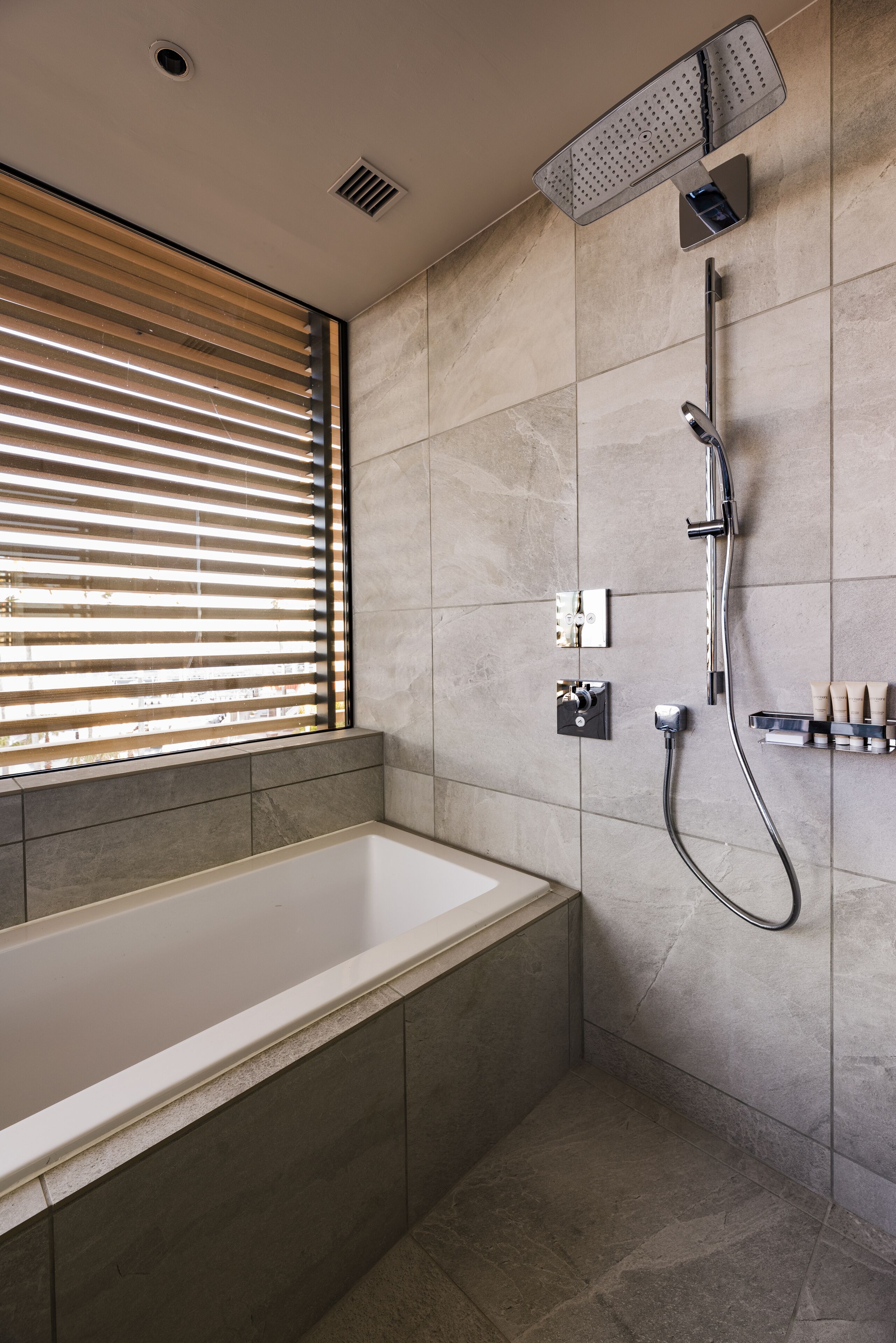 A modern bathroom with a bathtub, a showerhead, and a window with blinds.
