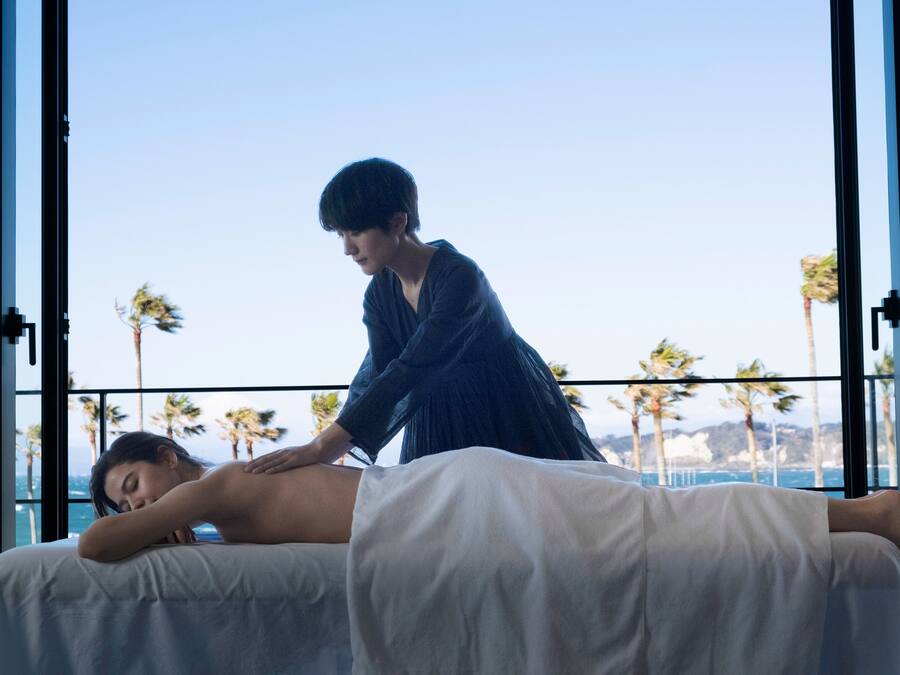 Massagebehandling på en balkon med udsigt til palmer og havet.