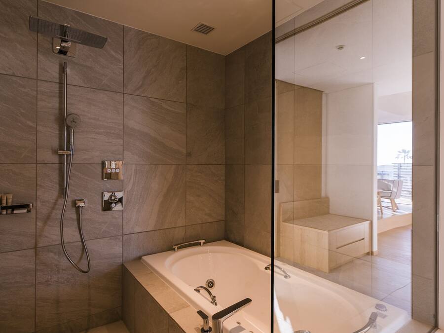 Un baño moderno con una bañera grande, zona de ducha y mampara de cristal.