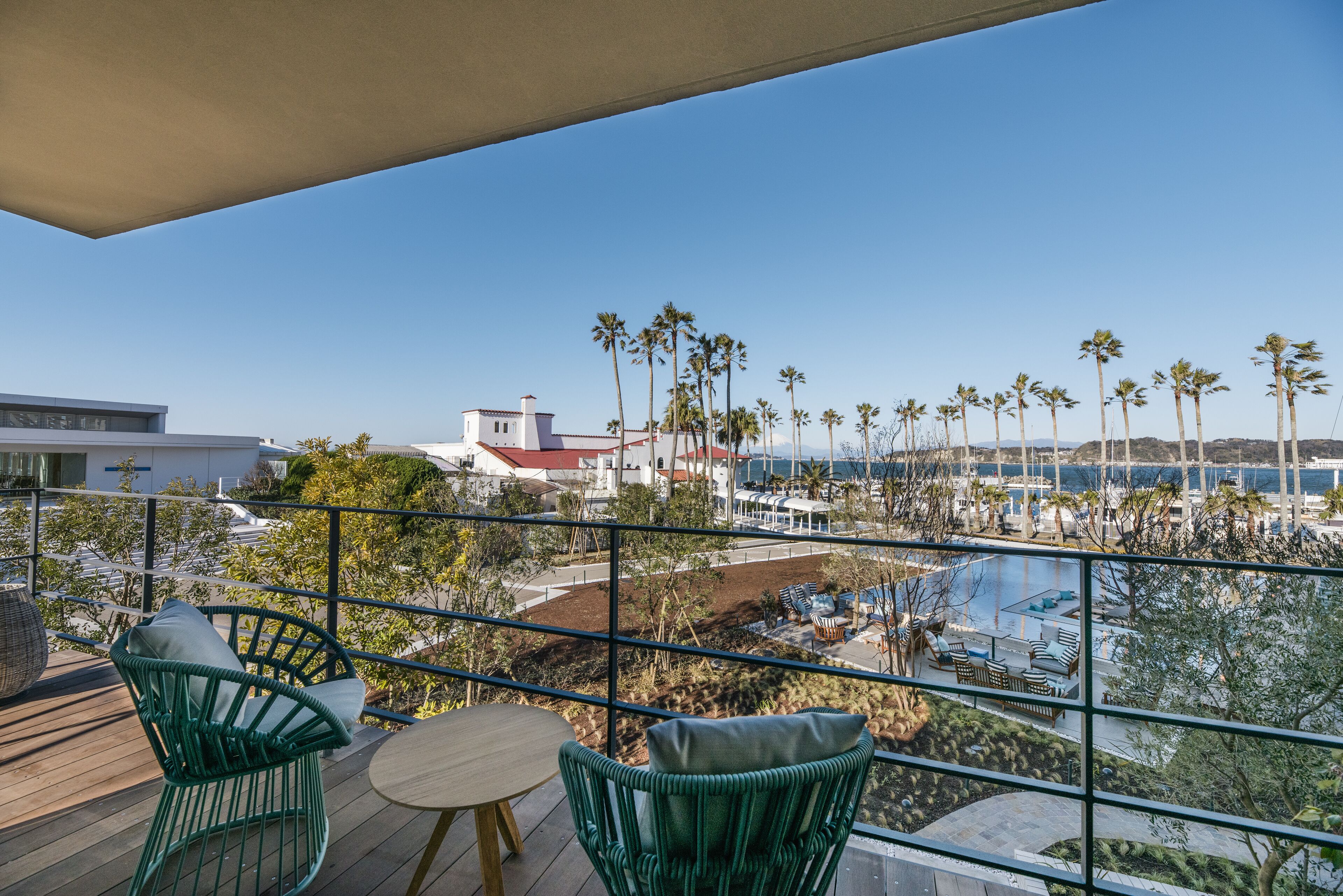 A balcony with wicker chairs, a small table, and a view of a pool and palm trees.