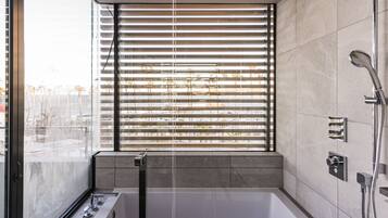 A modern bathroom with a large bathtub, a glass-enclosed shower, and a window with blinds.
