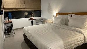 A hotel room with a large bed, a small table with a chair, a window with a view, and a ceiling light. - d'primahotel Bintan (Bintan)