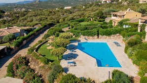 Une grande piscine entourée d’une végétation luxuriante, offrant une vue sur les montagnes lointaines et les immeubles résidentiels.