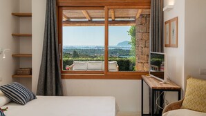 Une chambre avec une grande fenêtre, des poutres en bois, un lit, une table de chevet et un téléviseur.