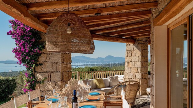 Une table en bois, dressée pour le repas, avec vue sur les montagnes et la mer.