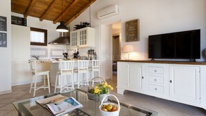 Een moderne keuken met witte kasten, een centraal eiland met barkrukken, een grote flatscreen-tv en een eetgedeelte met een glazen tafel.