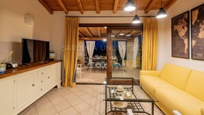 Een woonkamer met een houten plafond, een geel sofa, een glazen salontafel en een televisie op een houten kast.