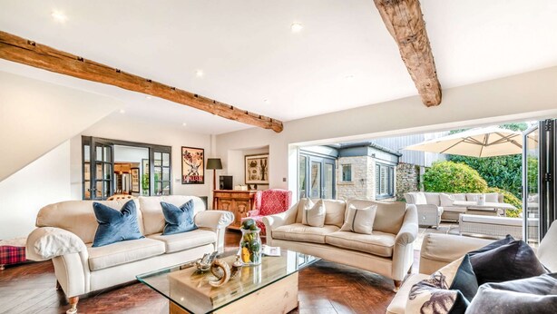 A spacious living room with a glass coffee table, two sofas, and a view of the garden through large windows.