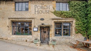 A stone building labeled "Porch House" with two windows, a door, and a small outdoor seating area.