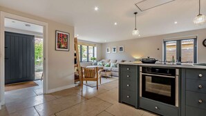 A modern kitchen with a central island, built-in oven, and a dining area with a wooden table and chairs. - Three bedroom Cotswold holiday cottage - Steeple View (Todenham)