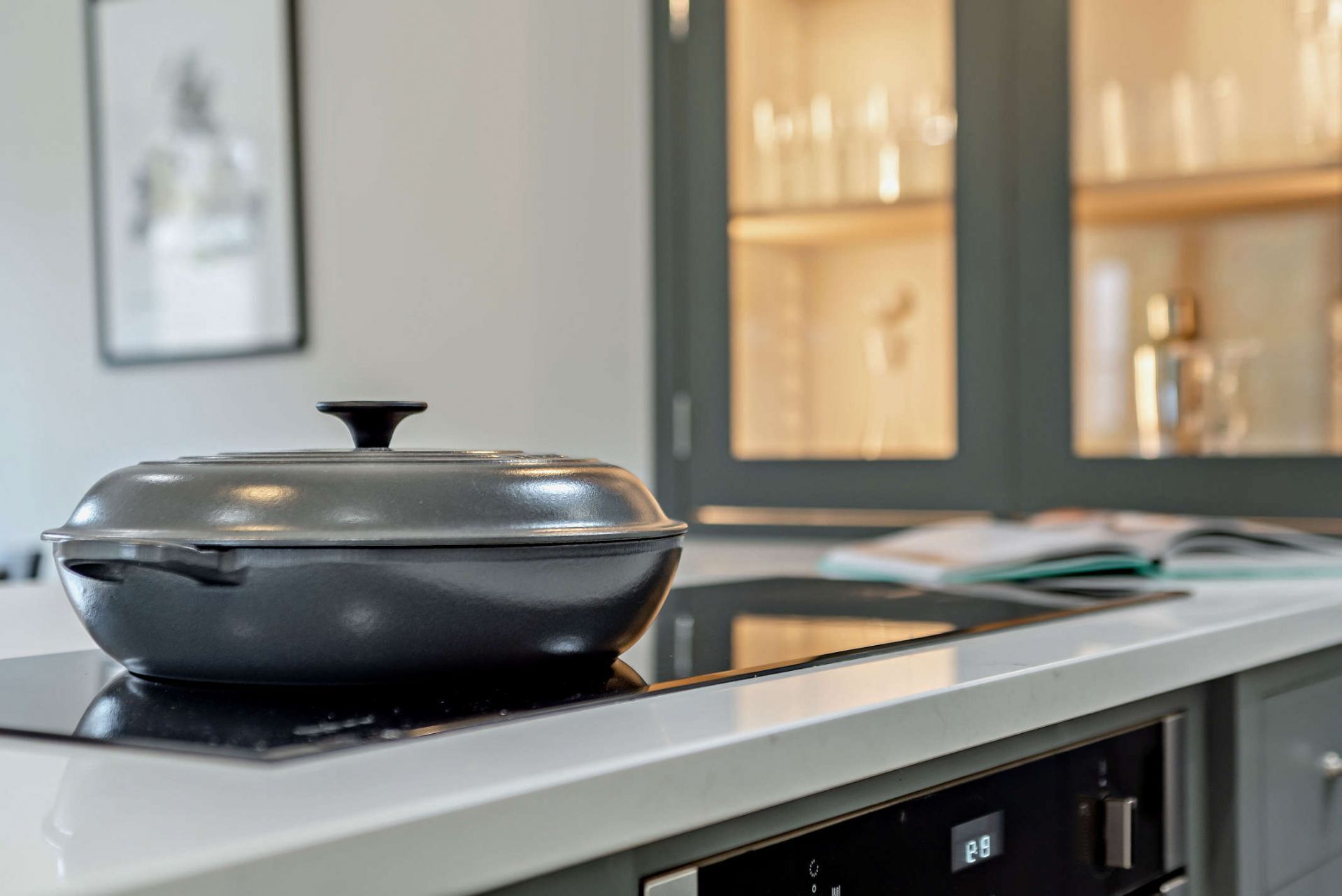 A kitchen with a modern stove, a digital clock, and a window with shelves of glassware.