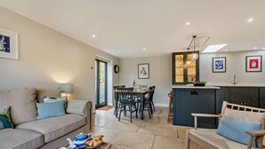 A modern living room with a sofa, a dining table, and a kitchen area with a bar. - Three bedroom Cotswold holiday cottage - Steeple View (Todenham)