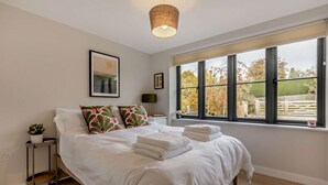 A bedroom with a large bed, a window with a view of trees, a hanging light fixture, and a framed picture on the wall. - Three bedroom Cotswold holiday cottage - Steeple View (Todenham)
