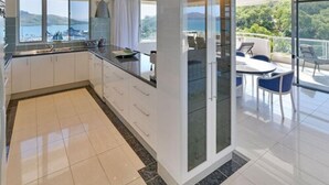 A modern kitchen with a view of the sea, a dining area with outdoor seating, and a balcony with a glass door.
