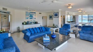 A spacious living room with a blue sofa set, a coffee table, and a dining area with chairs.