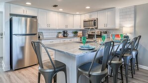 Une cuisine moderne avec des meubles blancs, des appareils en acier inoxydable et un îlot central doté de tabourets de bar.