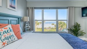 Une chambre d’hôtel avec un grand lit, une vue sur l’océan, une télévision et une plante.