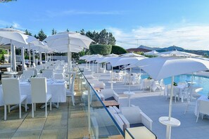 A rooftop terrace with white outdoor seating, umbrellas, and a pool.