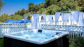 A hot tub with a white frame and a view of a pool area with blue umbrellas and white canopies.
