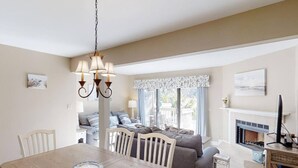 A dining area with a wooden table and chairs, a chandelier, and a view of a balcony with a sofa.