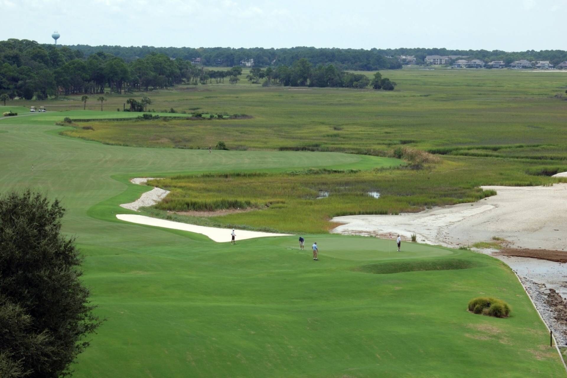 A golf course with sand bunkers, a water tower, and distant buildings.