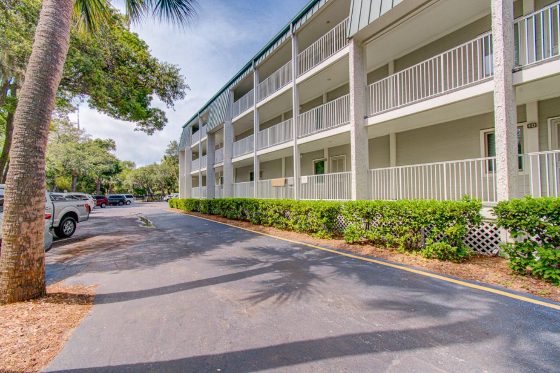 A multi-story hotel with balconies, a parking lot, and palm trees.