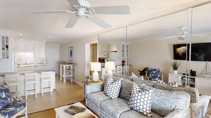Un salon moderne avec un canapé gris, des chaises blanches, une table à manger et une cuisine en arrière-plan.