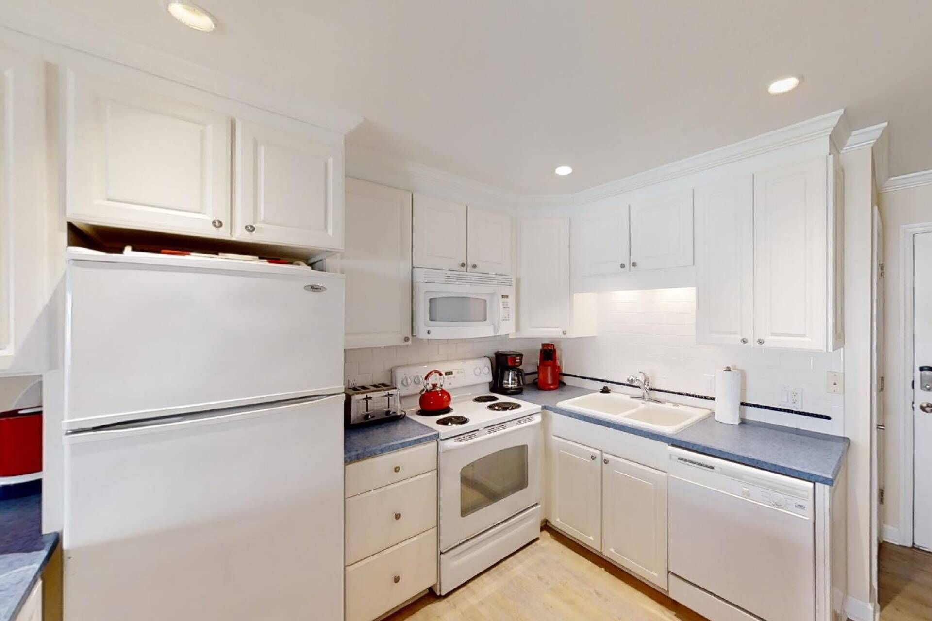 A compact kitchen with white cabinets, a microwave, a stove, a toaster, and a dishwasher.