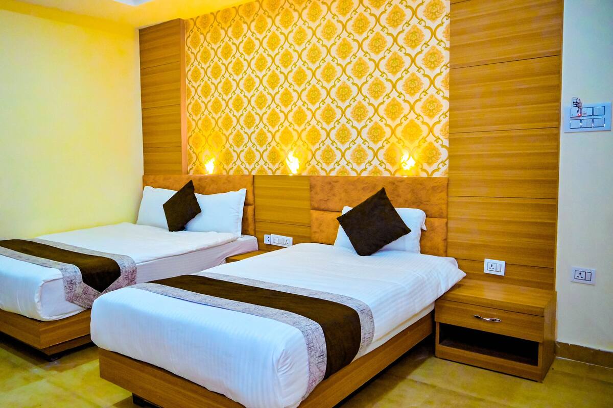A hotel room with two single beds, wooden headboards, a patterned wall, and a small wooden cabinet.
