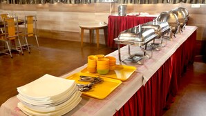Montaje de bufé con platos, tazones y cubiertos apilados sobre una mesa con mantel rojo.