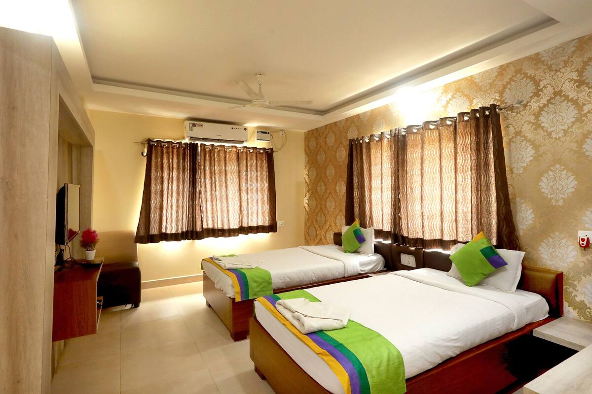 A hotel room with two beds, a desk, a chair, a TV, and a ceiling fan.