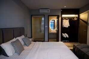A modern hotel room with a large bed, a walk-in closet, a bathroom with a glass shower, and a view of the city.